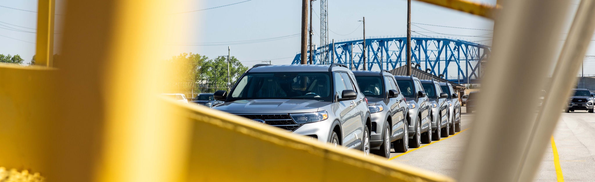 A partially blocked view of a line of cars parked and ready for automotive rail shipping.