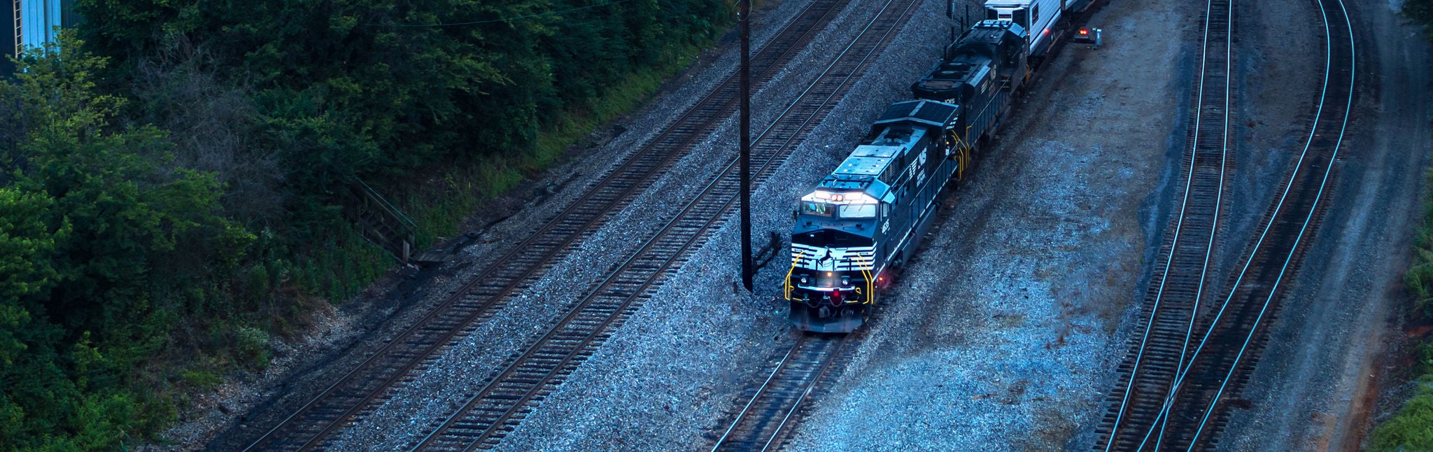 Locomotive driving down track with woods nearby, shipping metals by rail